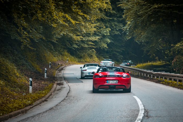 Porsches driving in the group on the open mountain road. Different models are on the photo, from the 911,944, 993 and Boxter models. This photo represent enthusiast driving during weekend and enjoying in mountain road and ride. Photo have vintage look and was taken on the cloudy day.